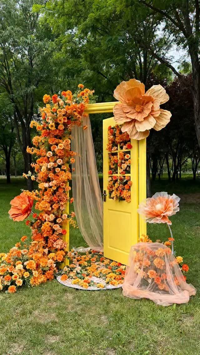 A yellow door frame decorated with orange flowers and large paper blooms in a garden.