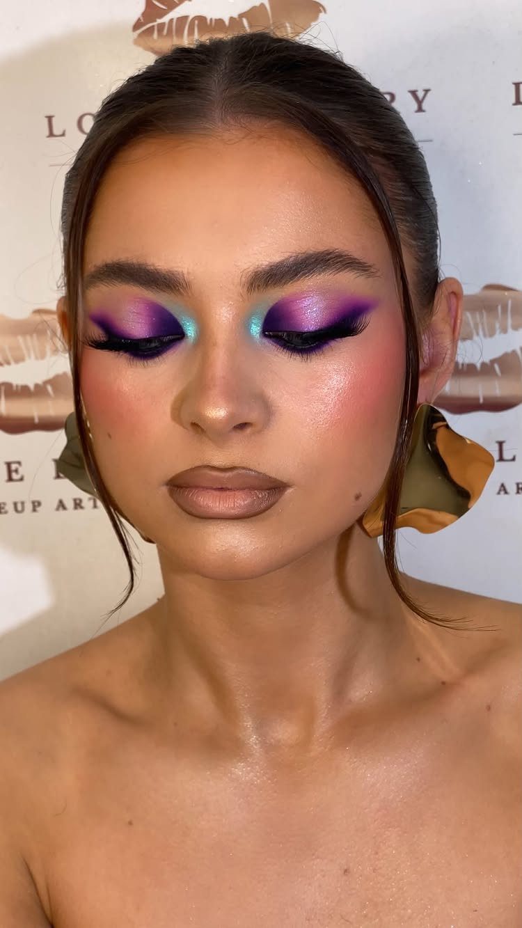 Woman with vibrant purple and teal eyeshadow, peach blush, and matte nude lips.