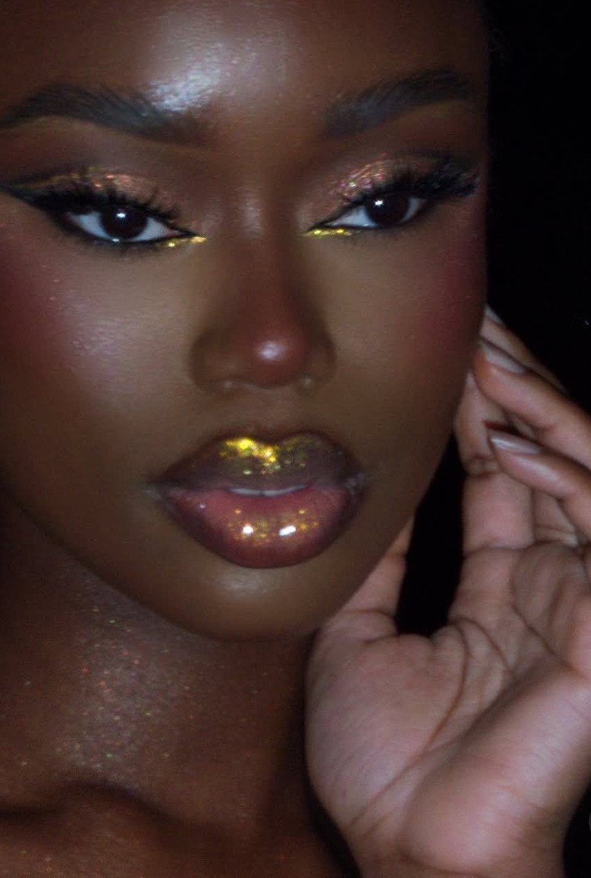 A person wearing glam makeup with gold glitter on the eyes, lips, and neck.