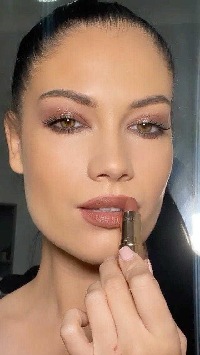 Woman applying a matte nude lipstick to her lips with a gold lipstick tube.
