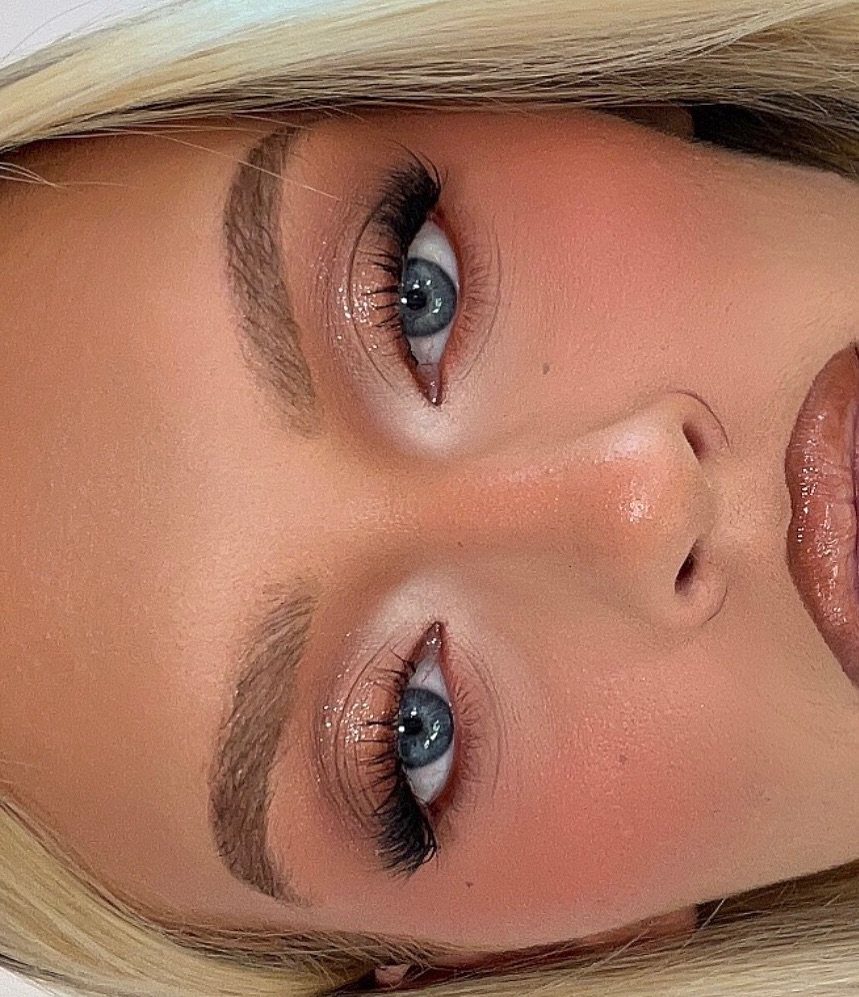 Close-up of a woman's face showing peach blush, groomed brows, and long eyelashes.