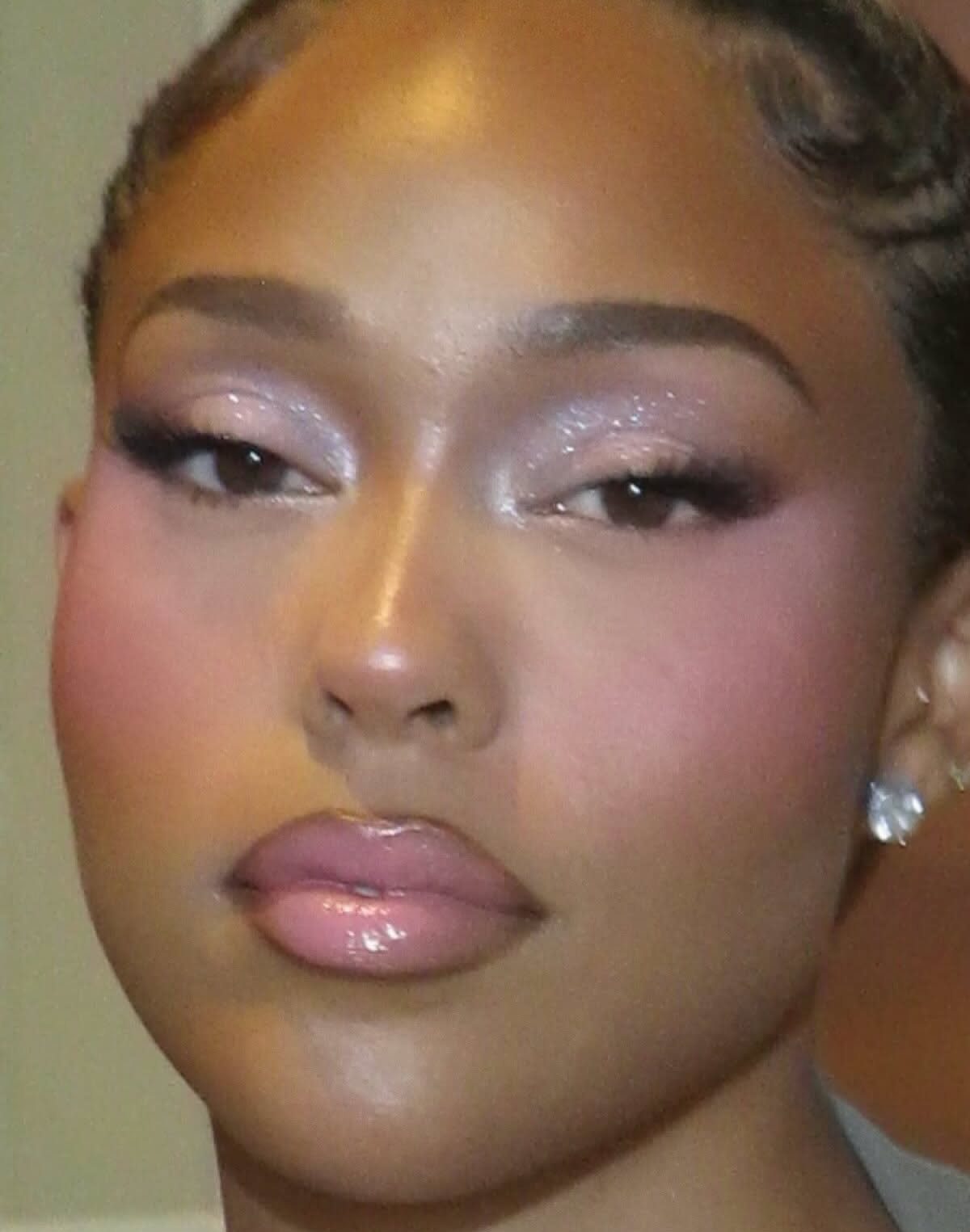 Woman with shimmering soft pink eyeshadow, glossy pink lips, and bright pink blush on her cheeks.