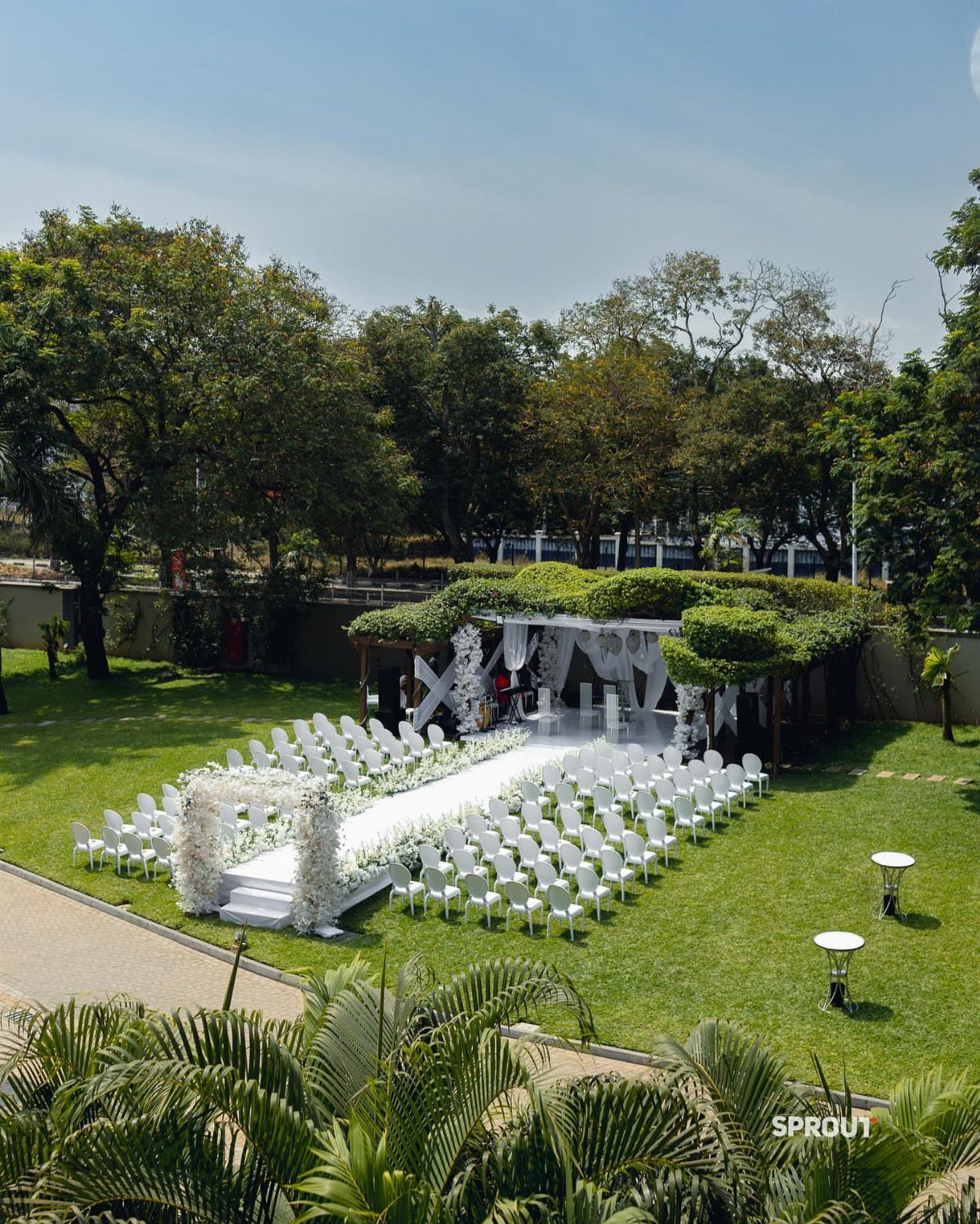 White wedding chairs and floral altar arranged on a green lawn in an outdoor venue.
