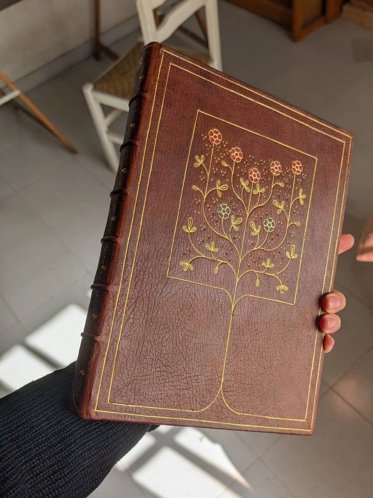 A person holding a decorative brown leather book with a gold embossed tree design.