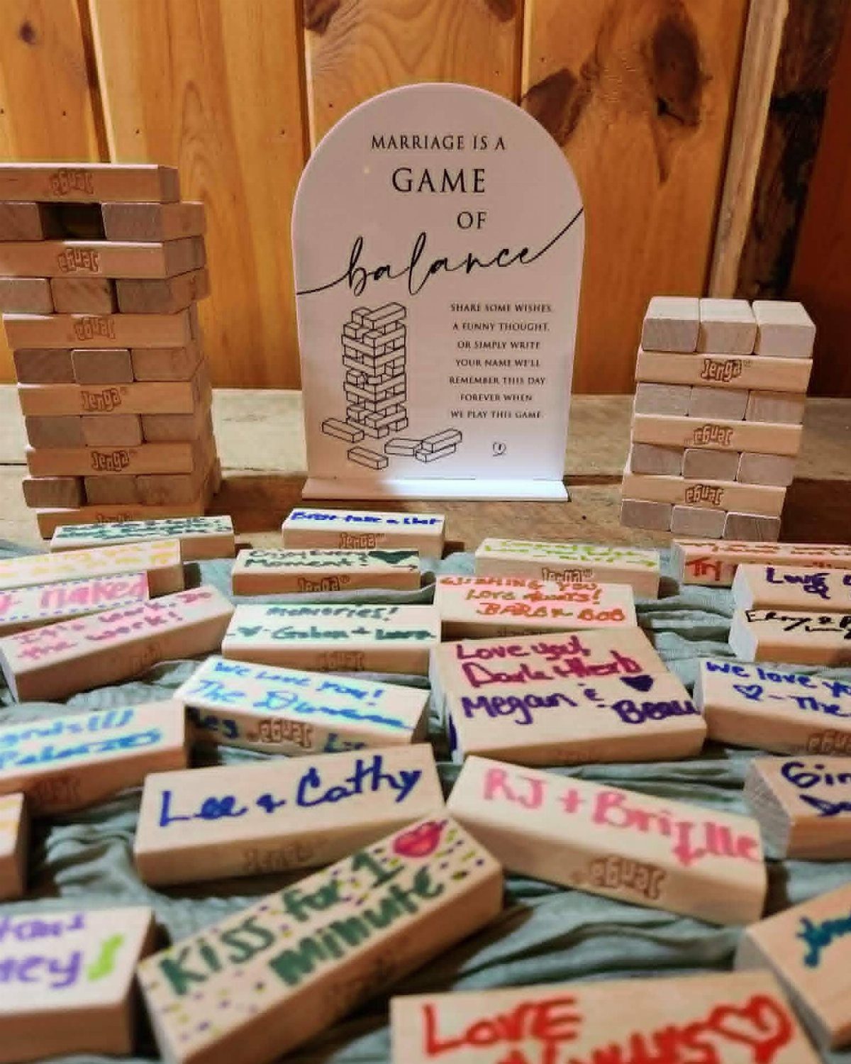 Wooden Jenga blocks with handwritten messages scattered on a blue cloth near a decorative sign.