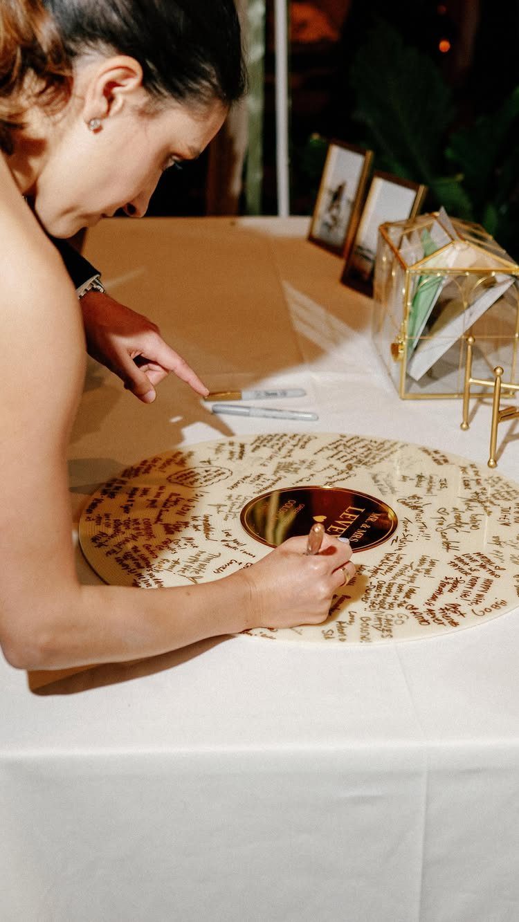 A woman writing her name on a circular wooden wedding guest book disc.