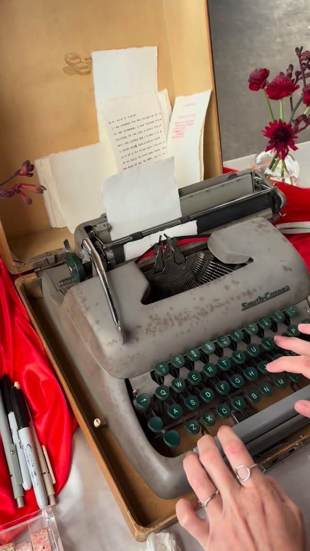 Hands typing on a vintage grey typewriter with several pieces of paper loaded into the machine.