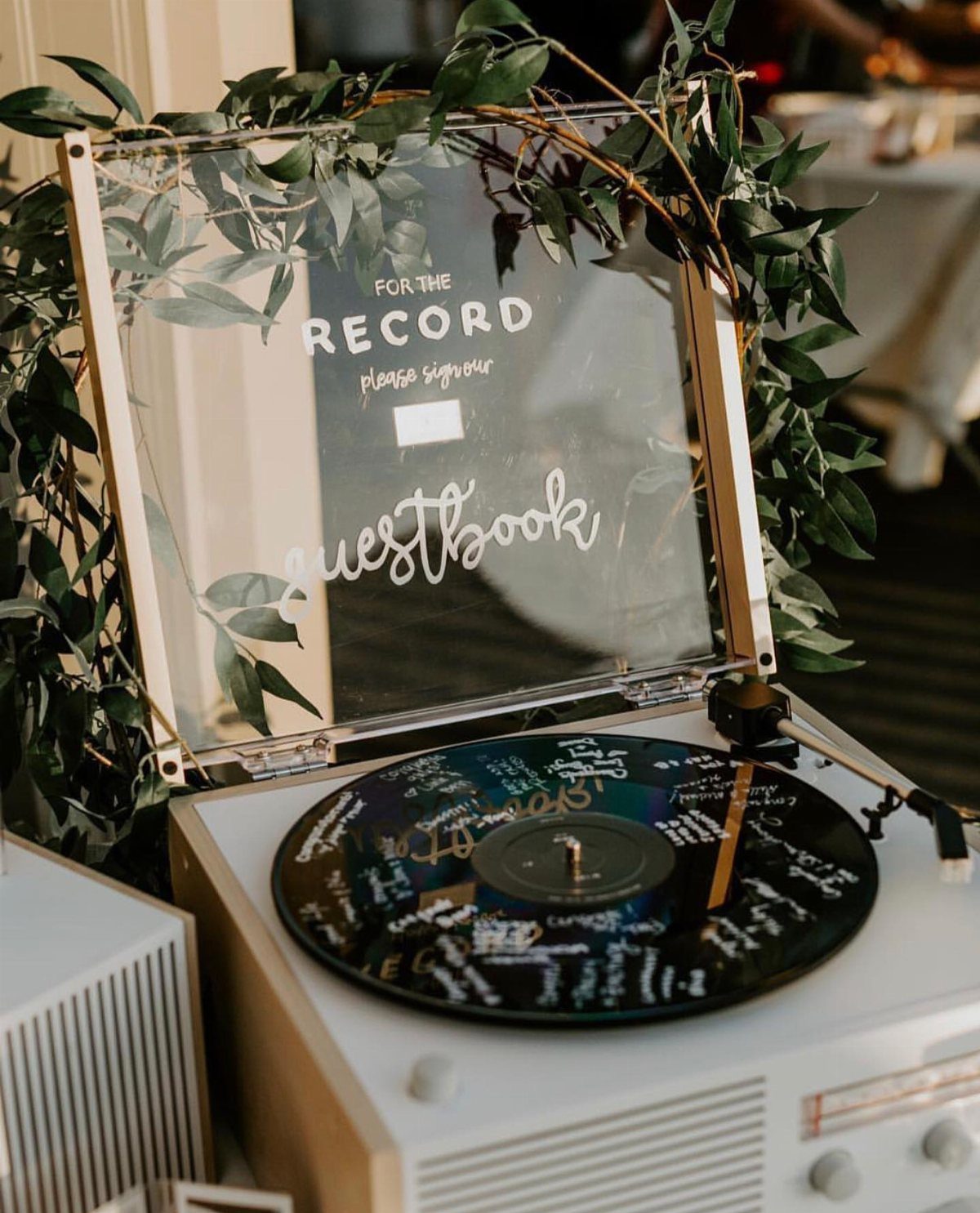 A signed vinyl record on a turntable with a clear acrylic sign and green leaves.