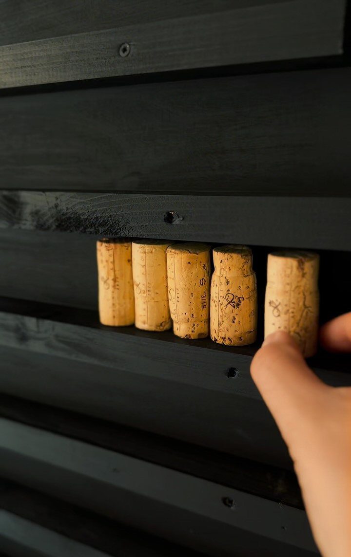 A hand placing a wine cork into a black wooden slatted guest book alternative.