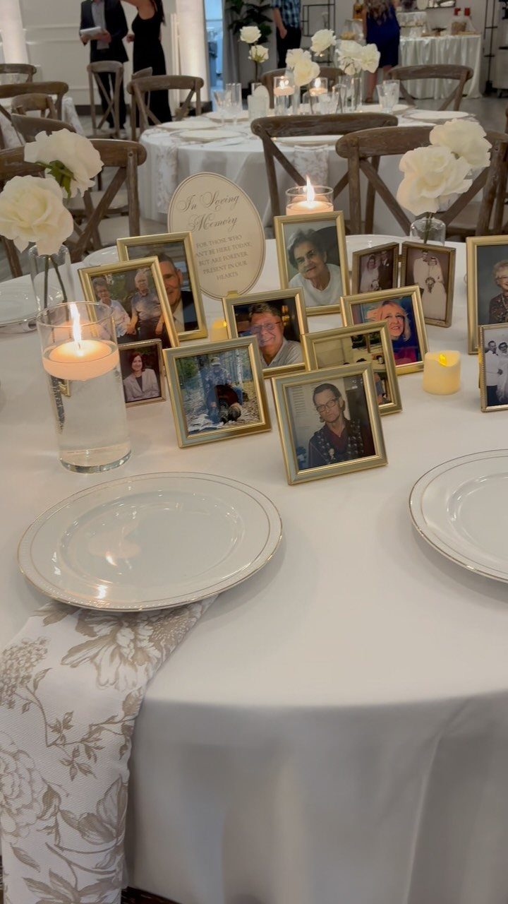Gold framed photographs and white roses arranged on a wedding table with memorial signage and candles.