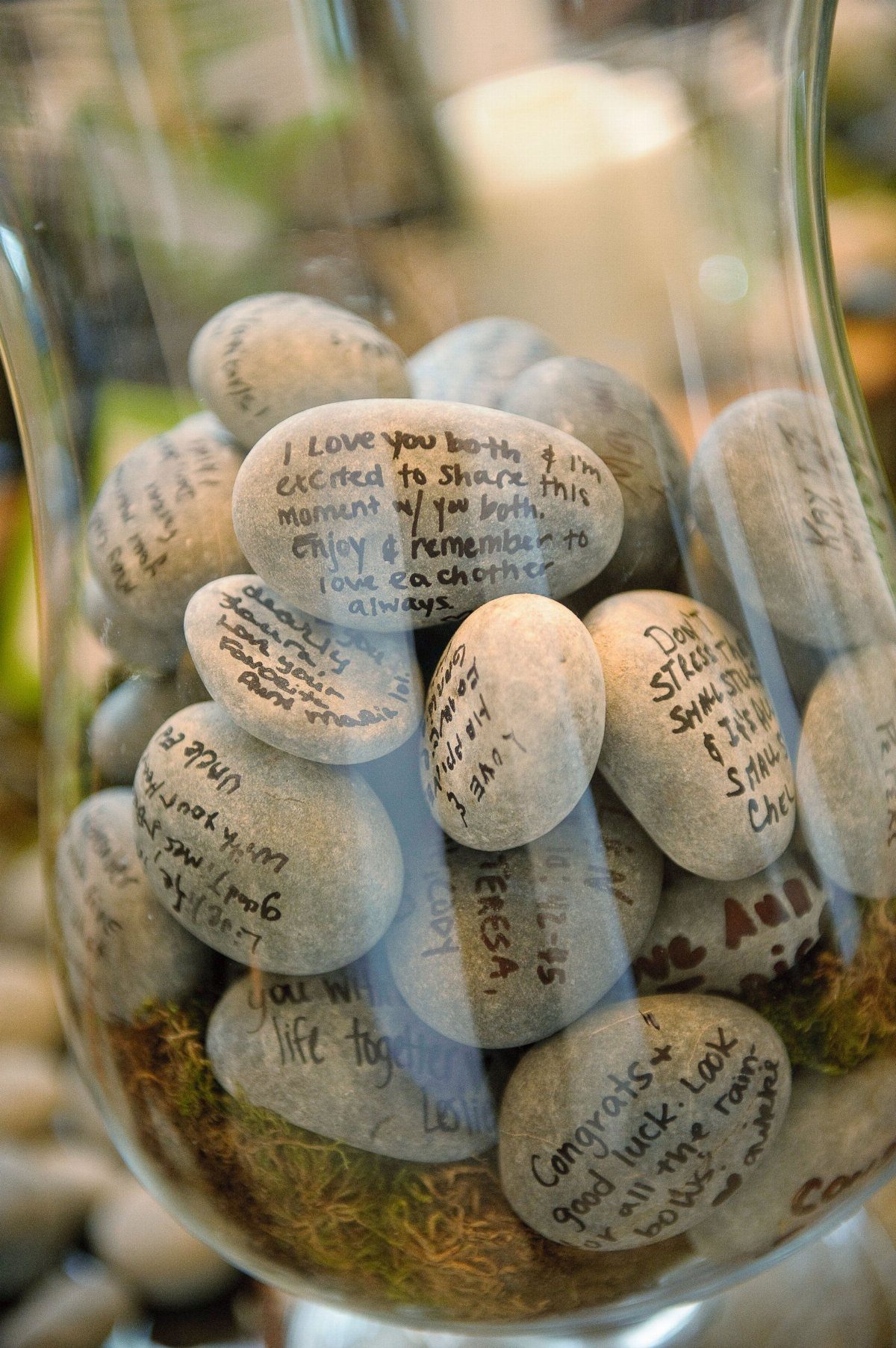 Handwritten messages on smooth stones inside a clear glass vase filled with green moss.