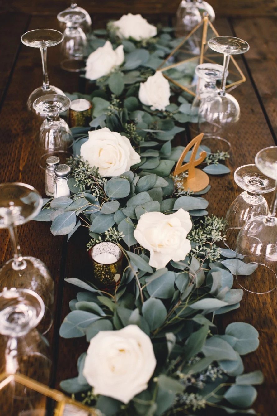 Eucalyptus greenery and white roses arranged as a long table runner on a wooden surface.