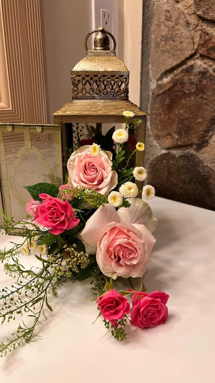 A gold vintage lantern decorated with pink roses and small white flowers on a white table.