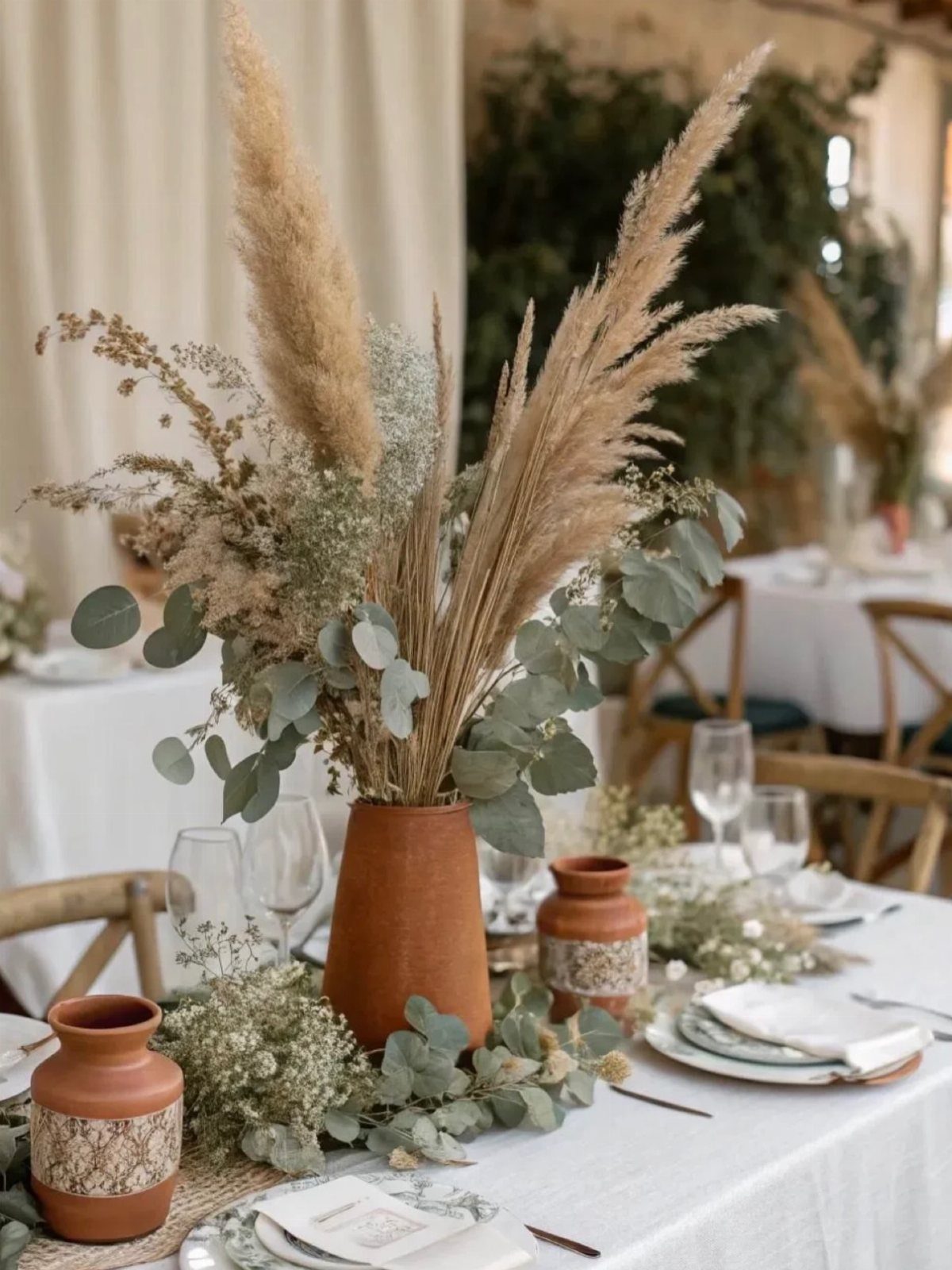 Terracotta vases filled with pampas grass and eucalyptus on a white wedding table setting.