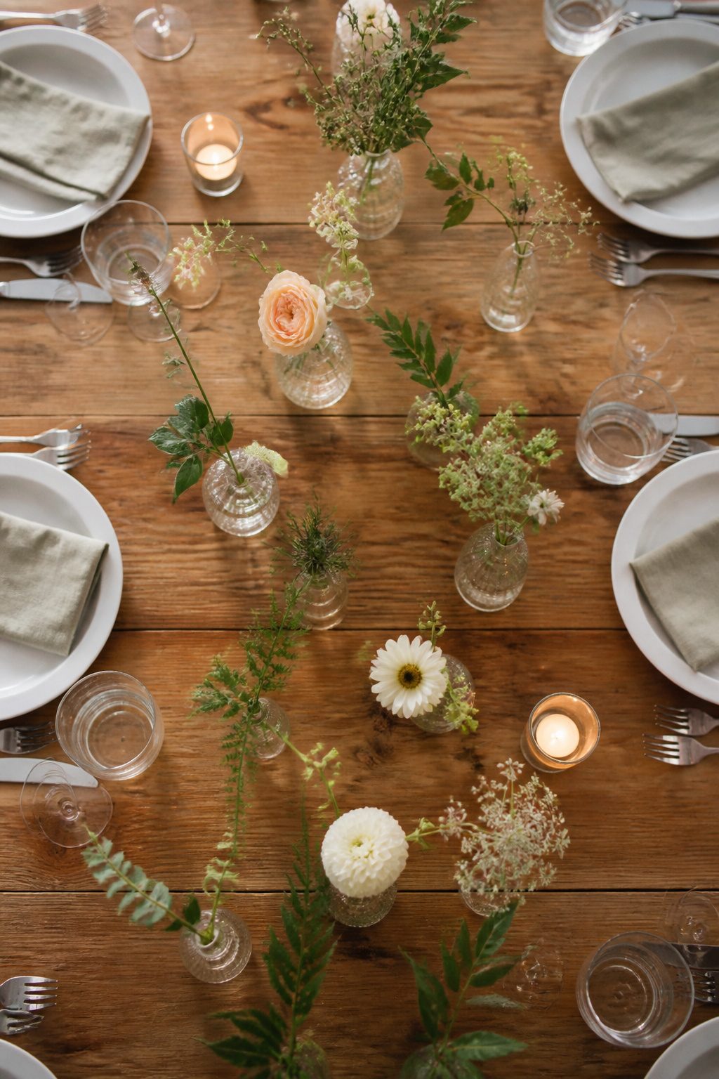 Several small bud vases filled with flowers arranged on a table.