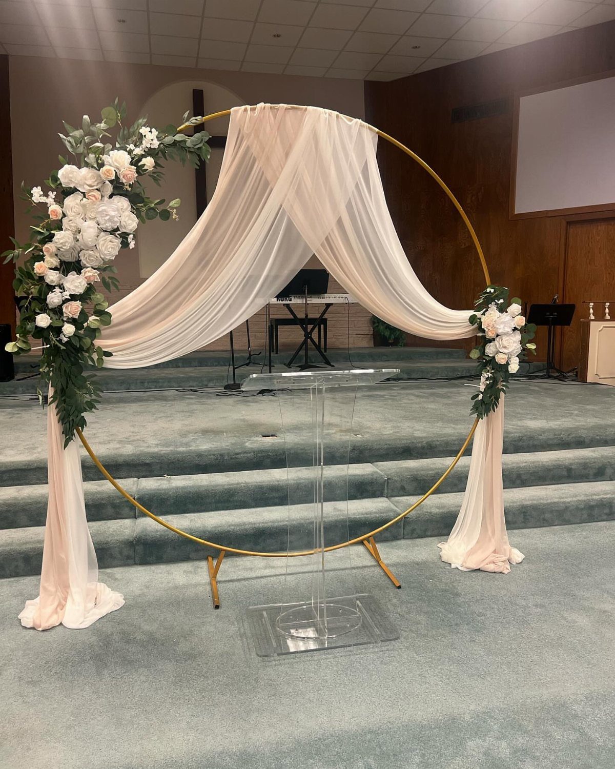 A gold circular wedding arch draped in pink fabric and decorated with white flowers and greenery.
