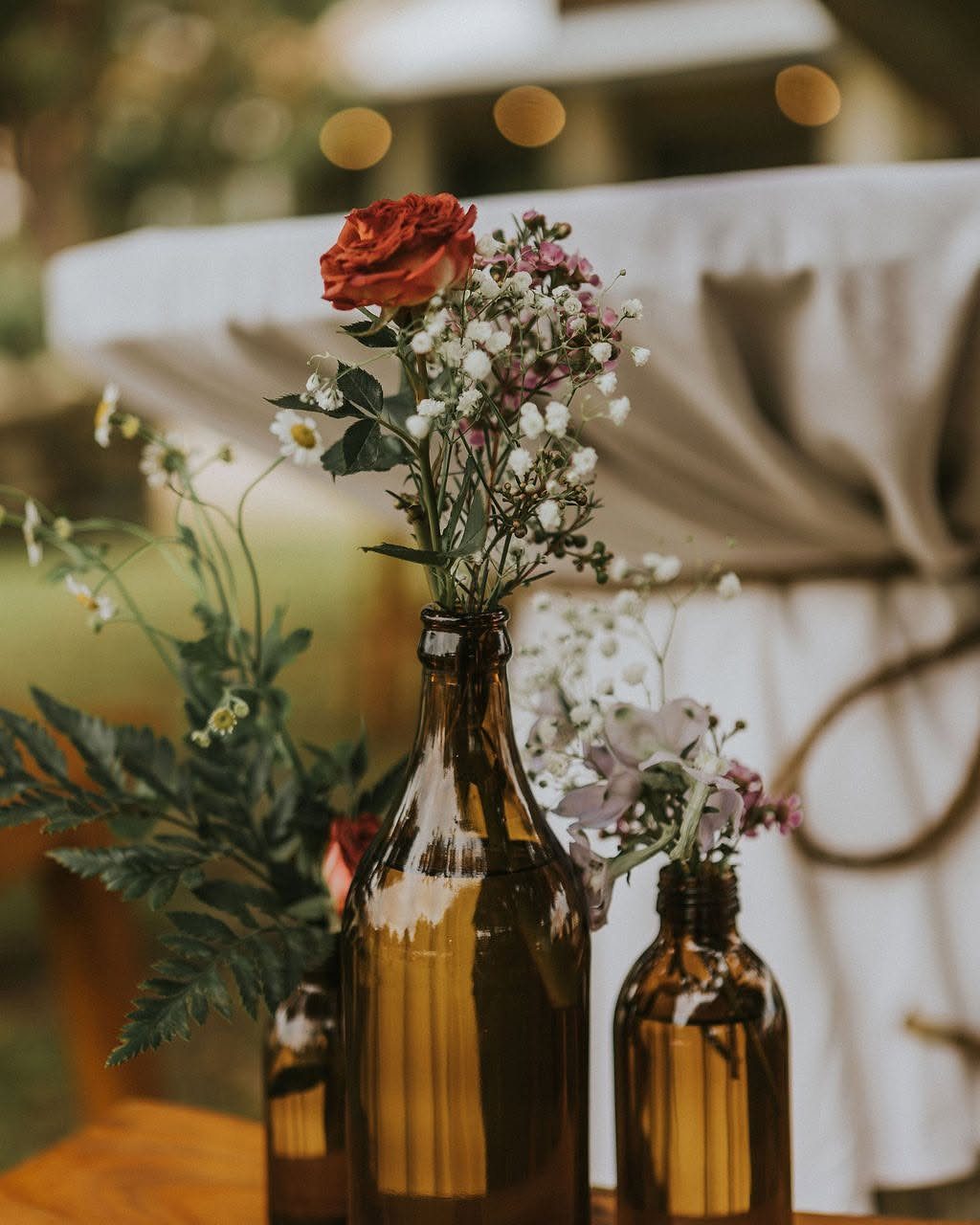 Amber glass bottles filled with colorful wildflowers and greenery on a wooden table.