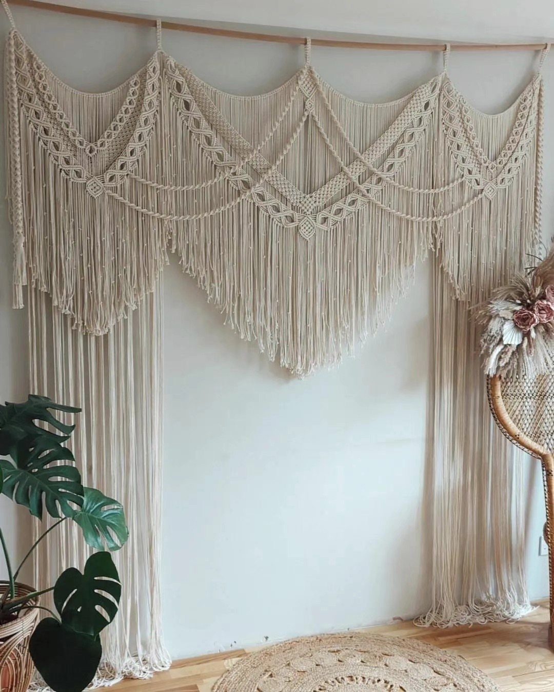 Large cream macrame wall hanging with intricate knot patterns and long fringe hanging from a wooden rod.