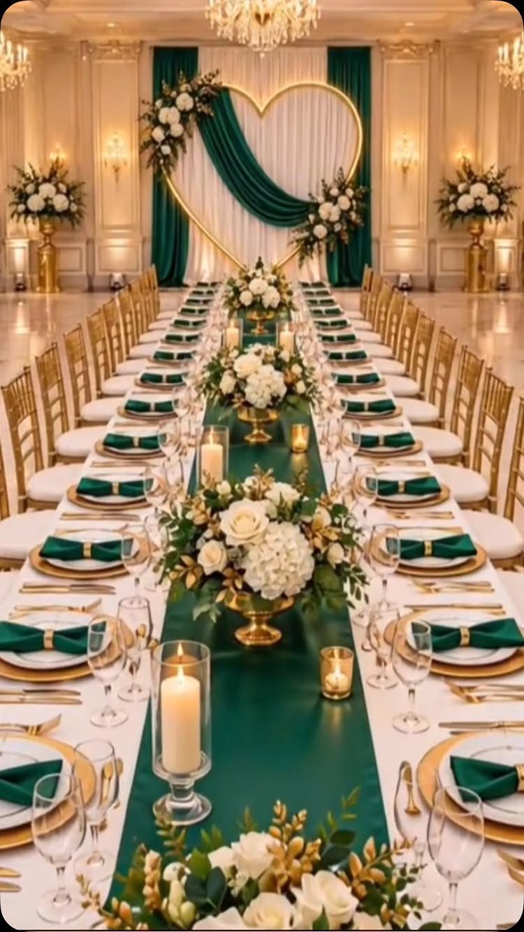 A long wedding reception table decorated with emerald green runners, gold chargers, and white floral arrangements.