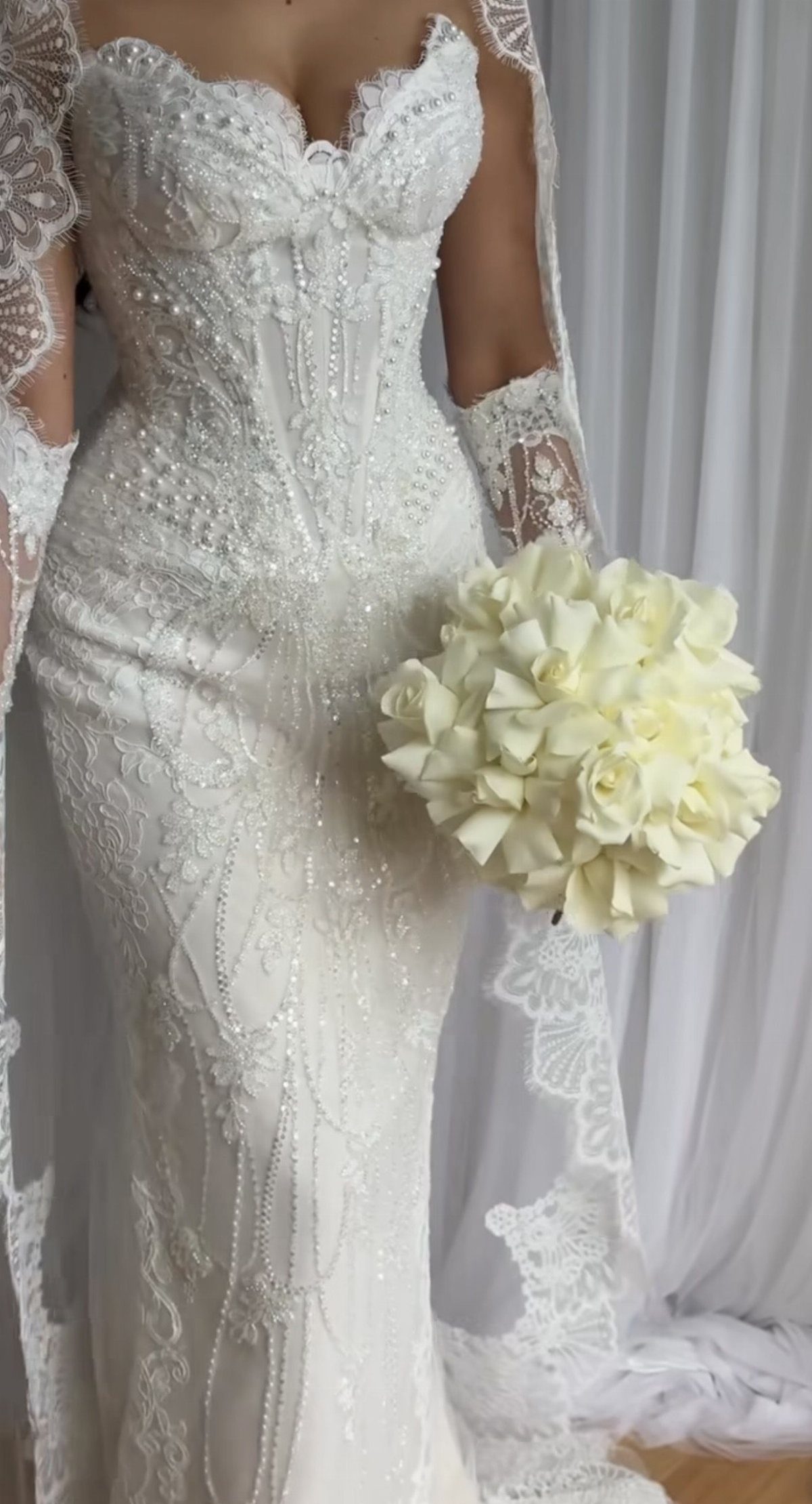 Tight Lace Wedding Dress: 8 Fitted Styles to Shape the Day 5 A woman in a beaded white lace wedding dress holding a bouquet of white roses.