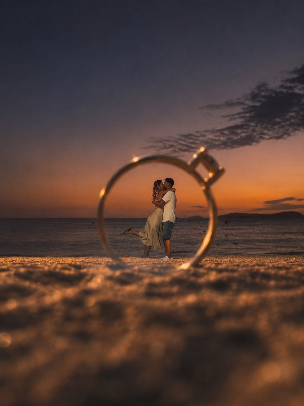 A couple kissing on a beach at sunset framed by a large ring silhouette.