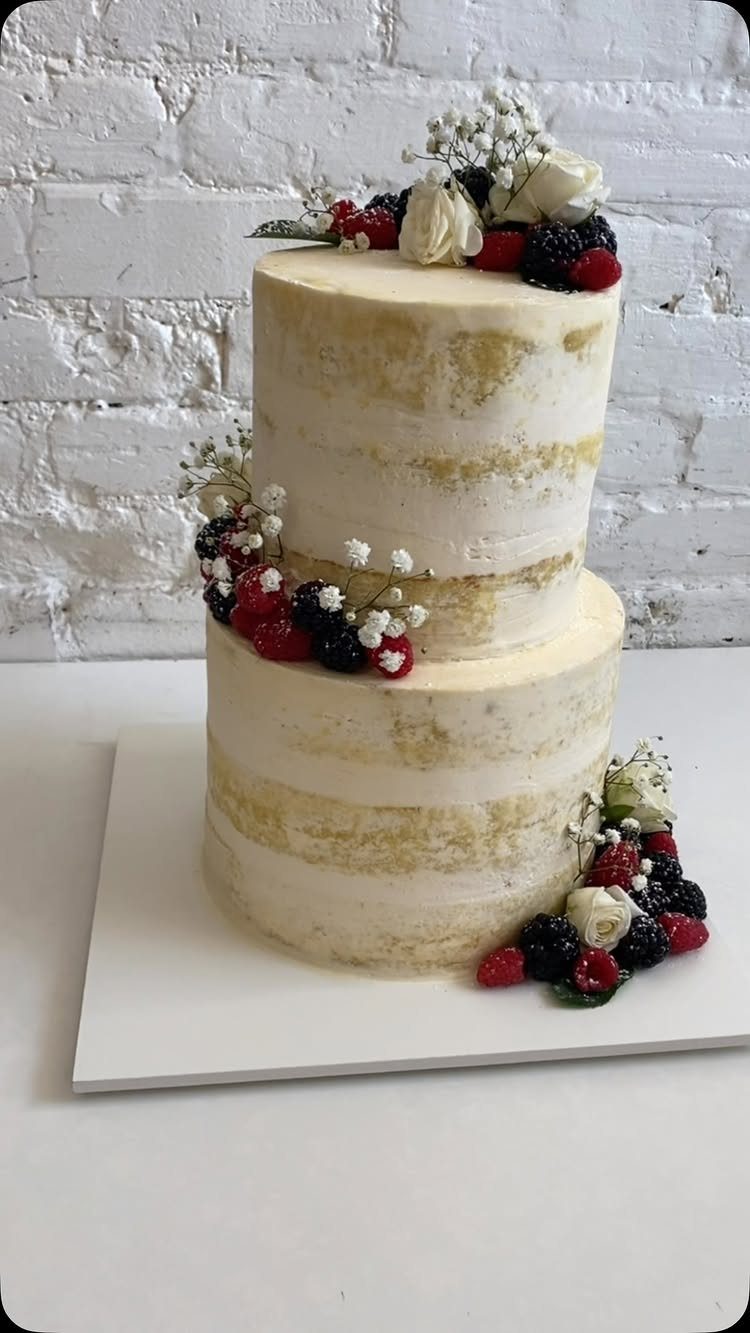 A two-tier semi-naked wedding cake decorated with white roses, berries, and baby's breath.