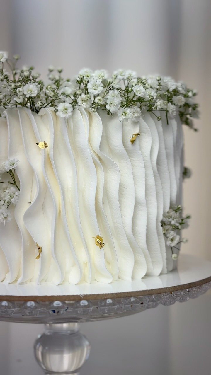 White ruffled buttercream wedding cake decorated with baby's breath flowers and gold leaf accents.