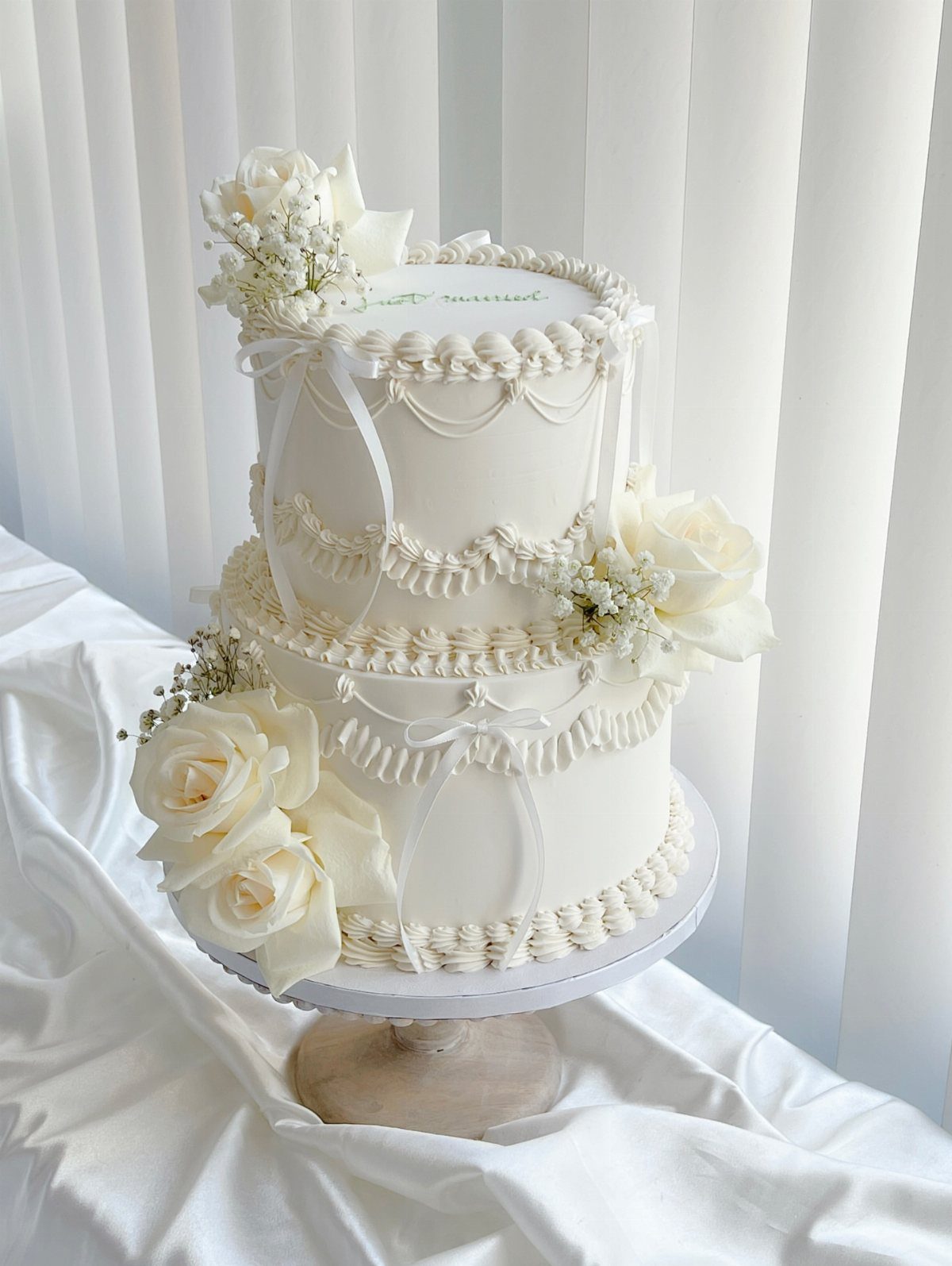 A two-tier white wedding cake decorated with fresh white roses and delicate white ribbons.
