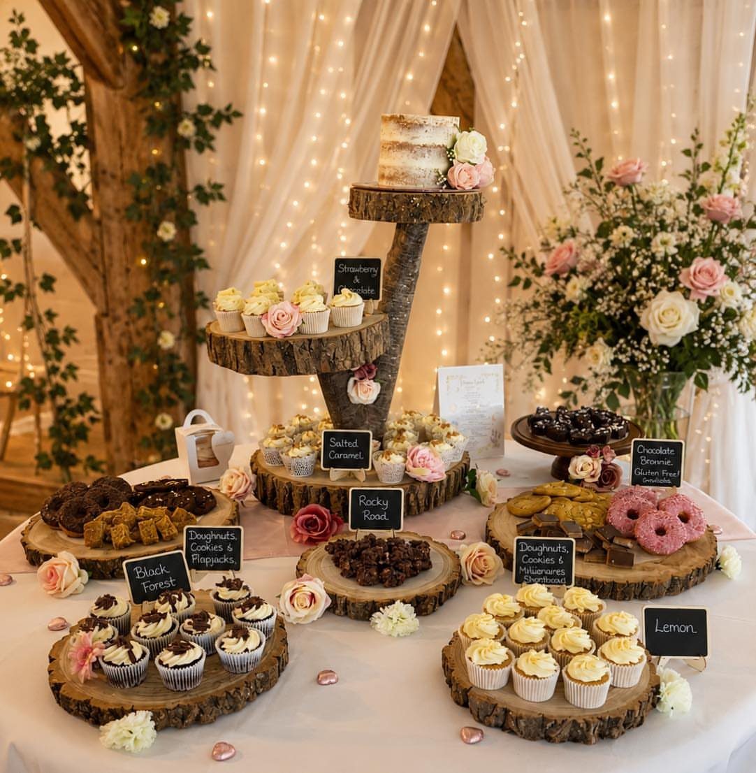 Various cupcakes and small cakes arranged on rustic natural wood slice stands on a decorated dessert table.