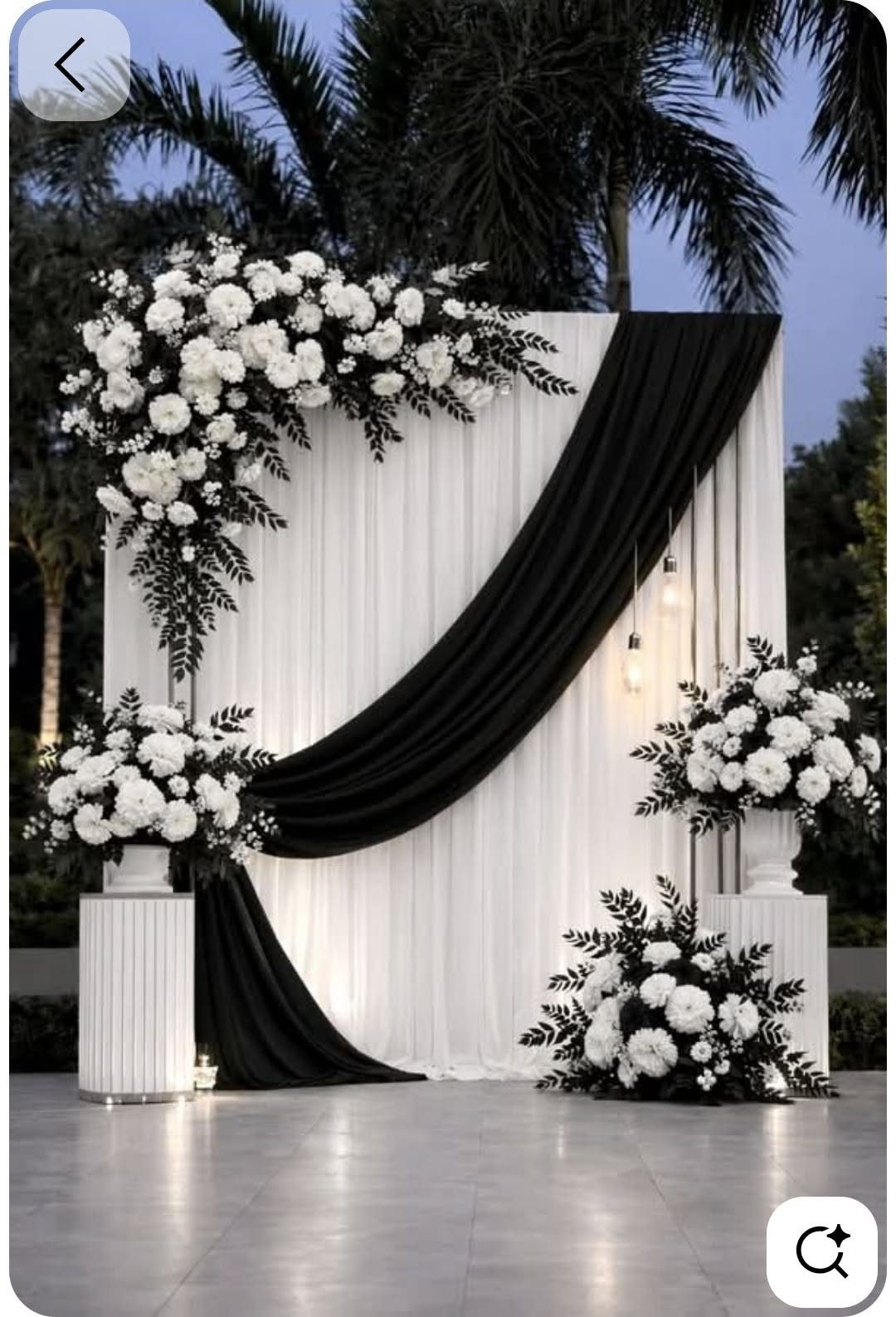 White and black draped fabric backdrop decorated with lush white floral arrangements and greenery.