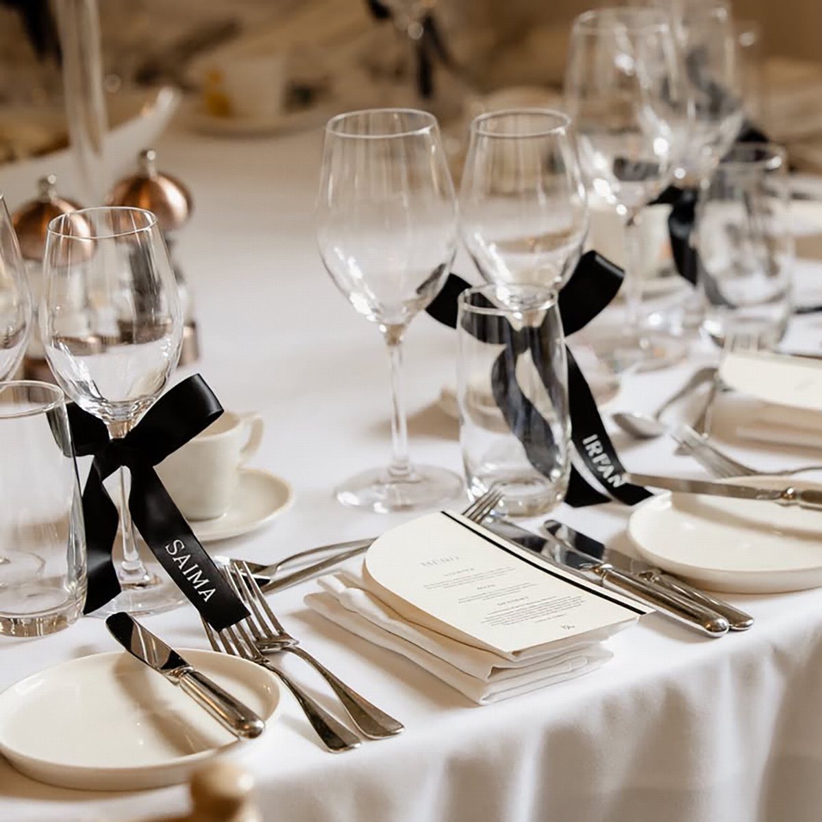 Wine glasses with black satin ribbons tied around the stems on a white wedding table.