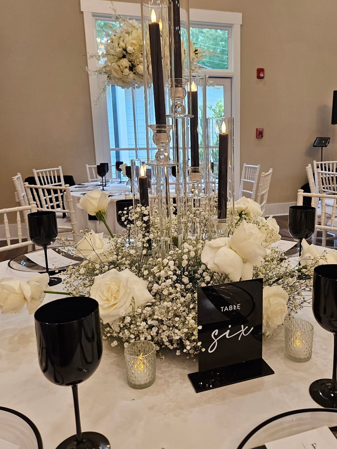 Black taper candles in a glass candelabra surrounded by white roses and baby's breath.