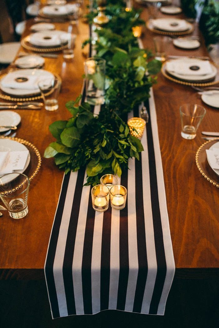 A black and white striped table runner decorated with green leaves and small glowing candles.