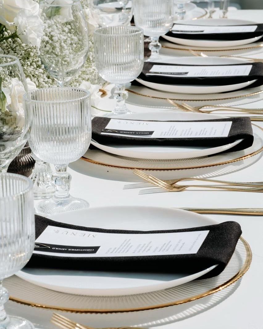 Gold cutlery and white plates with black napkins arranged on a formal wedding table setting.