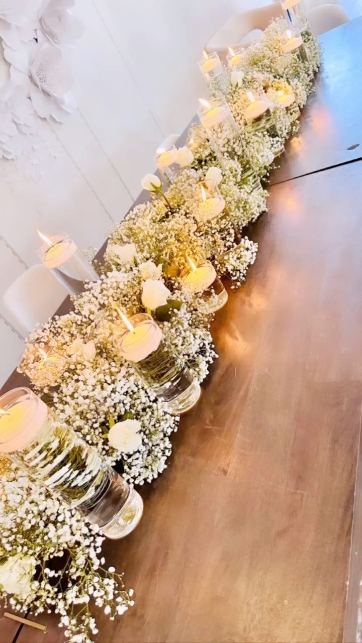 White baby's breath and rose floral centerpiece with lit tea light candles on a wooden table.
