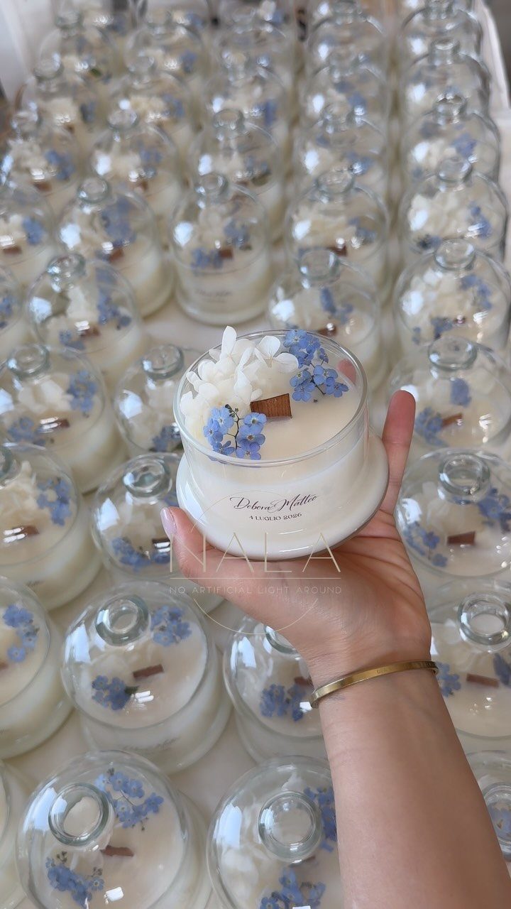 A hand holding a small glass jar candle decorated with tiny blue flowers.