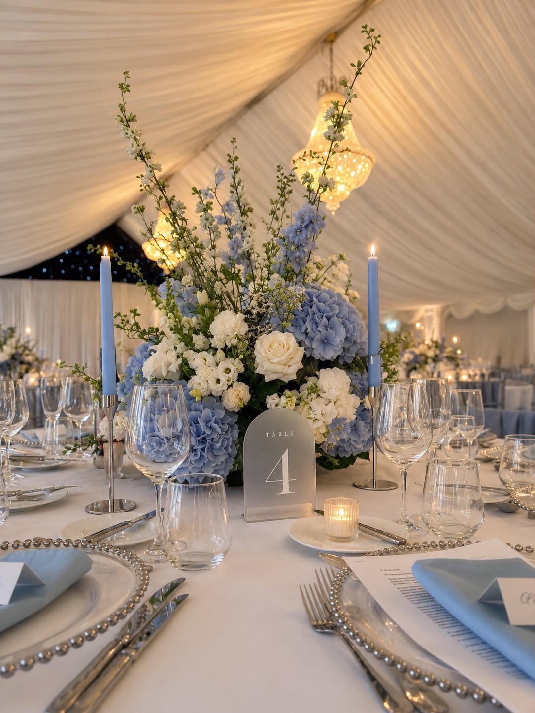 A wedding table decorated with powder blue flowers, blue taper candles, and elegant glassware.