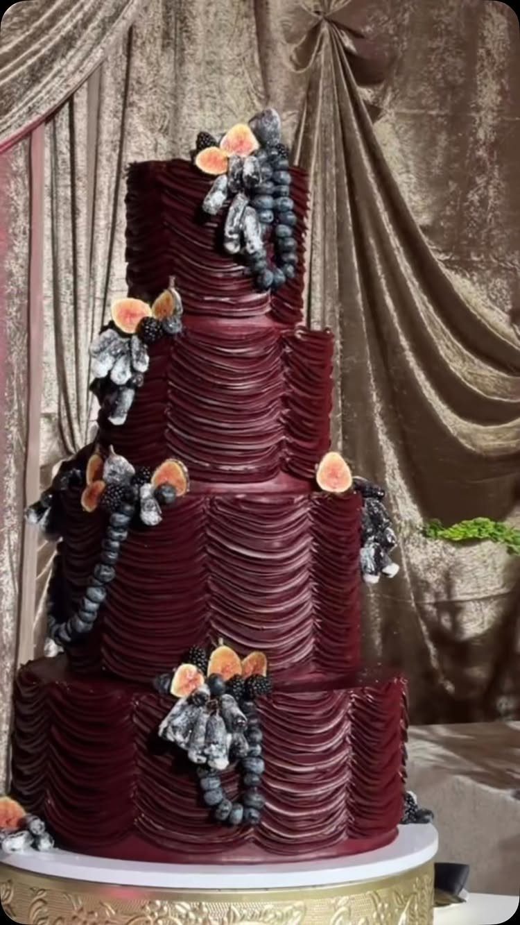 A four-tier burgundy ruffled wedding cake decorated with dark grapes and peach slices.