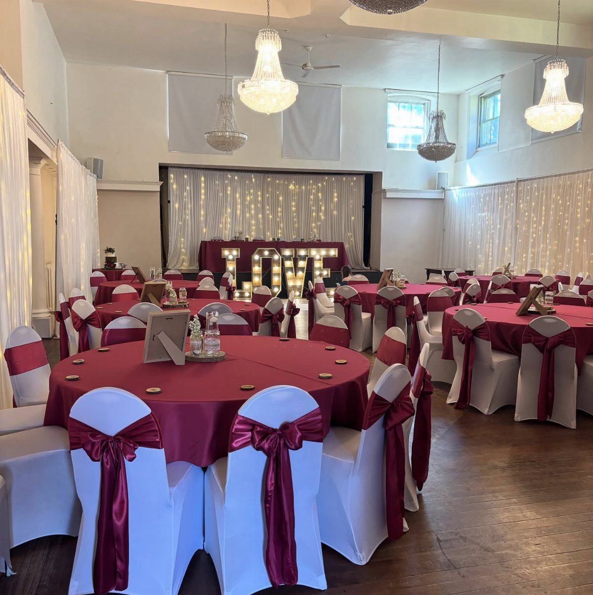 White wedding chairs decorated with large burgundy satin bows in a reception hall.