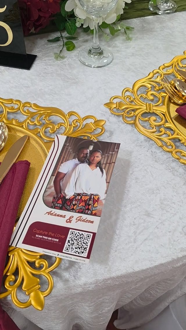 Gold chargers and burgundy napkins on a white tablecloth with floral arrangements.