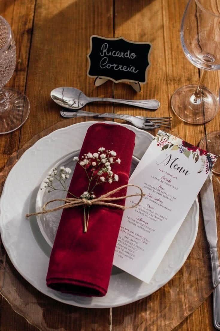 A rolled burgundy napkin tied with twine and baby's breath on a white plate.