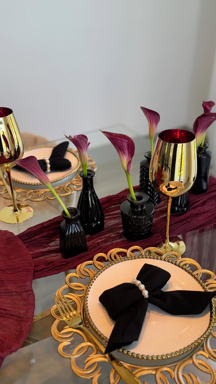 Burgundy calla lilies in black vases arranged on a table with burgundy runners and gold accents.