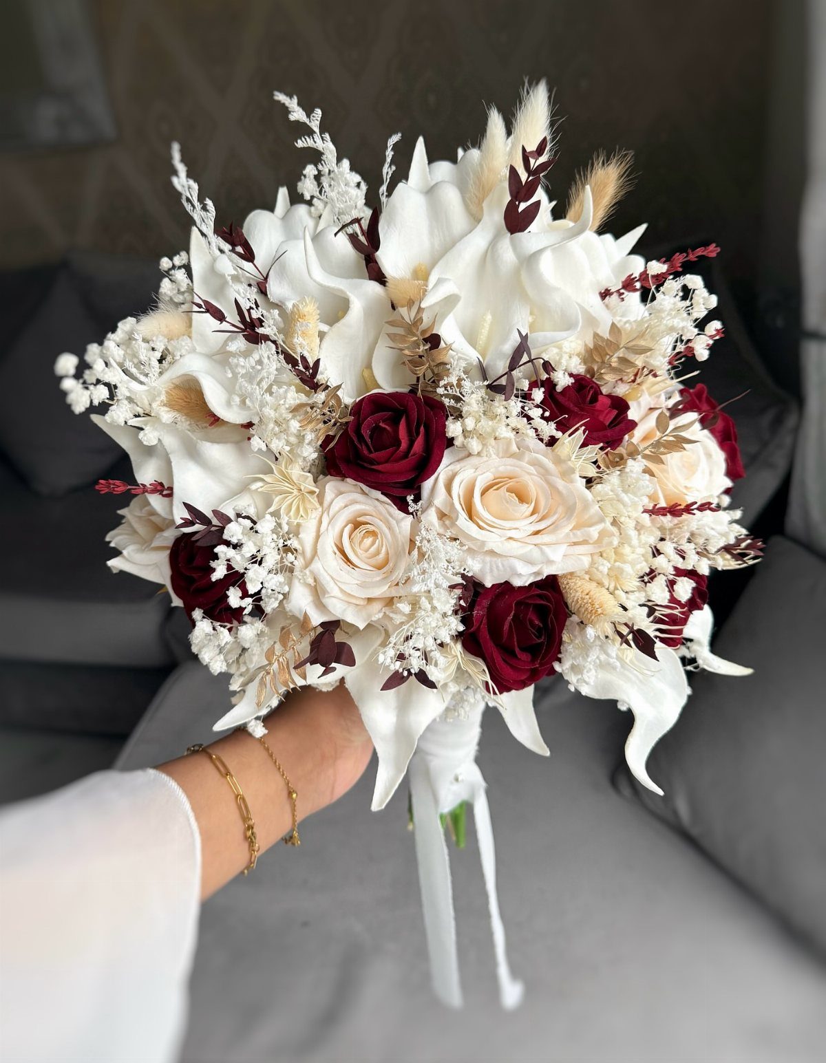 A hand holding a wedding bouquet with white calla lilies, cream roses, and burgundy roses.