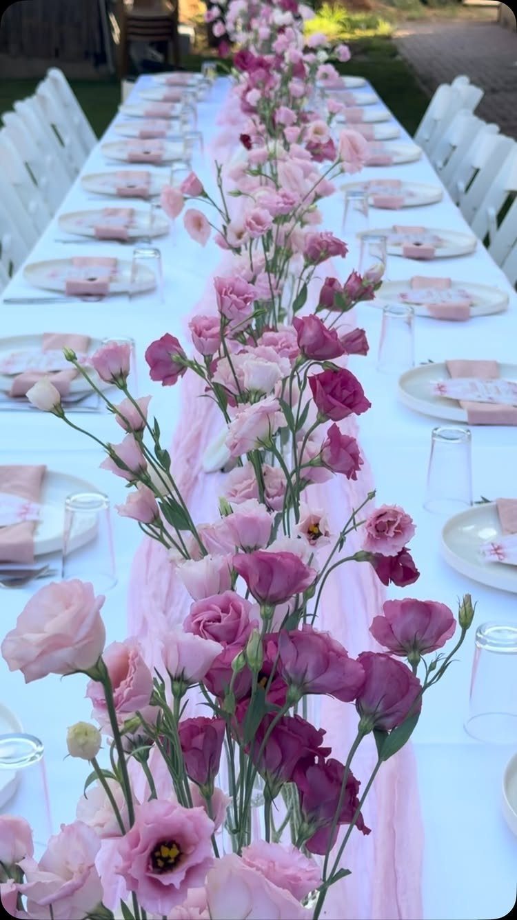 Pink and purple lisianthus flowers form a long runner down a white wedding reception table.
