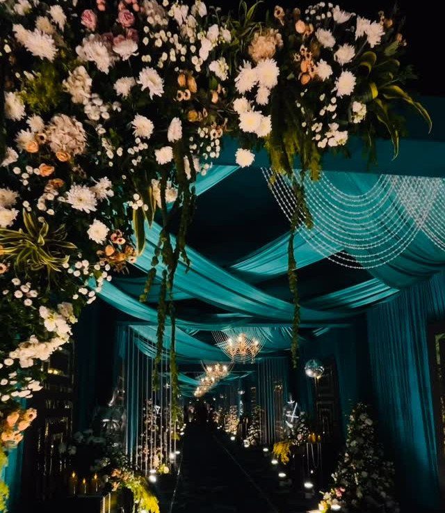 A grand wedding entrance with teal fabric draping, crystal strands, and lush white floral arrangements.