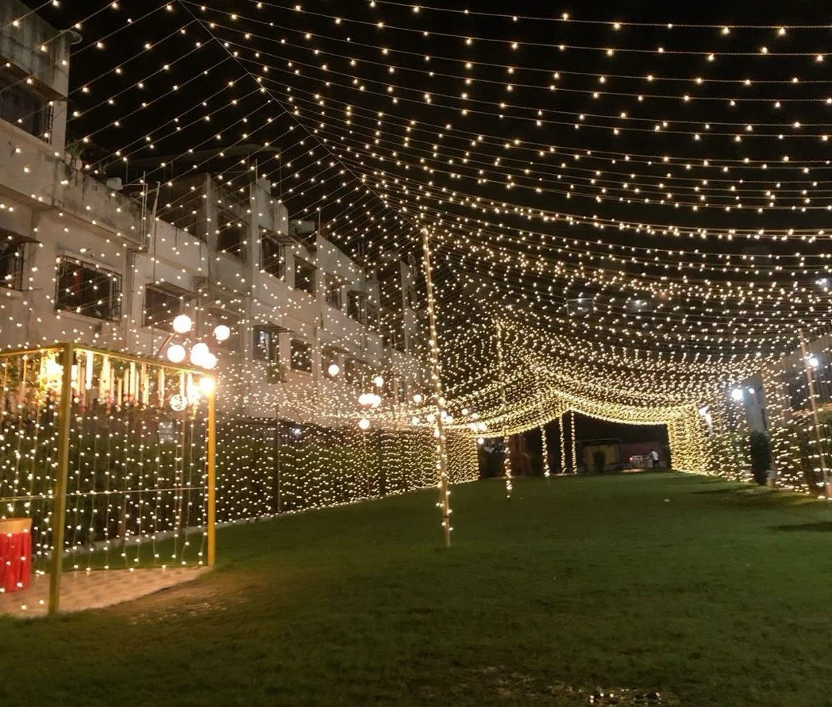 Strings of warm fairy lights draped across a dark night sky over a grassy outdoor lawn.