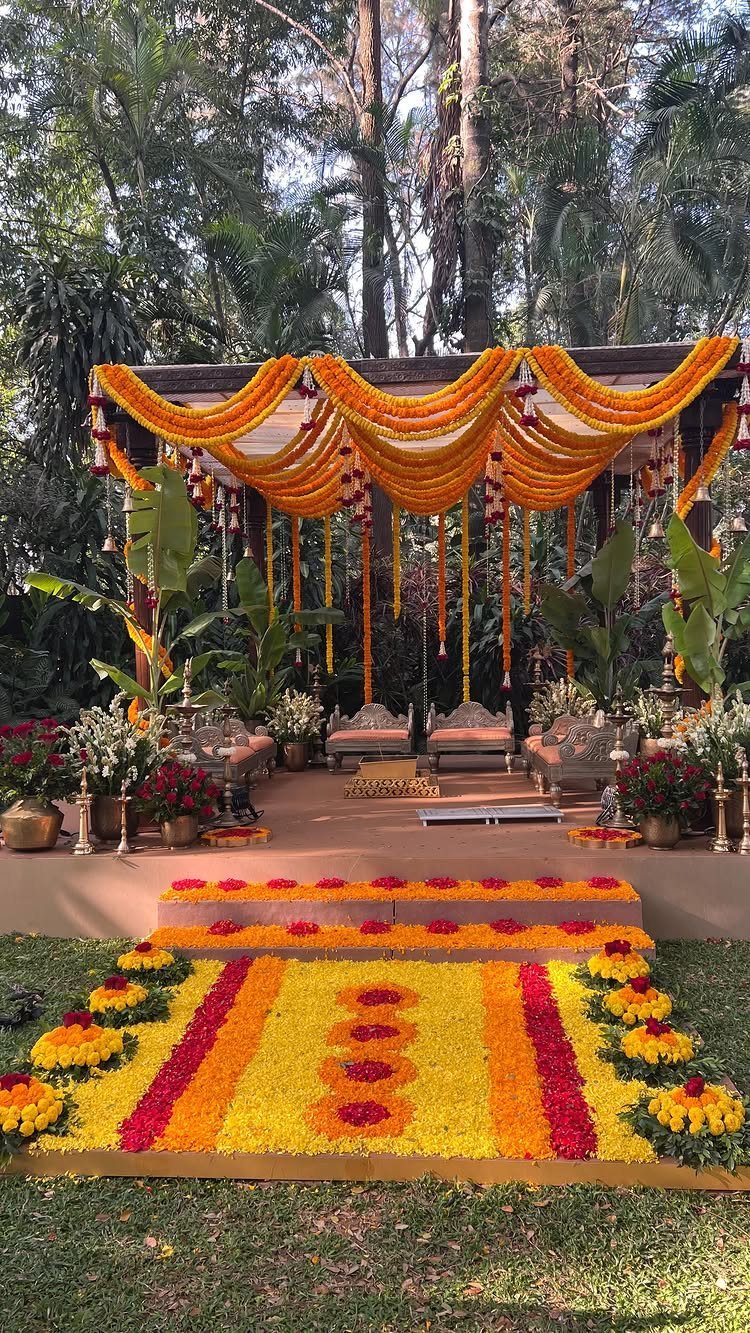 Marigold flower garlands decorating an outdoor wedding mandap with a colorful floral rangoli on the ground.