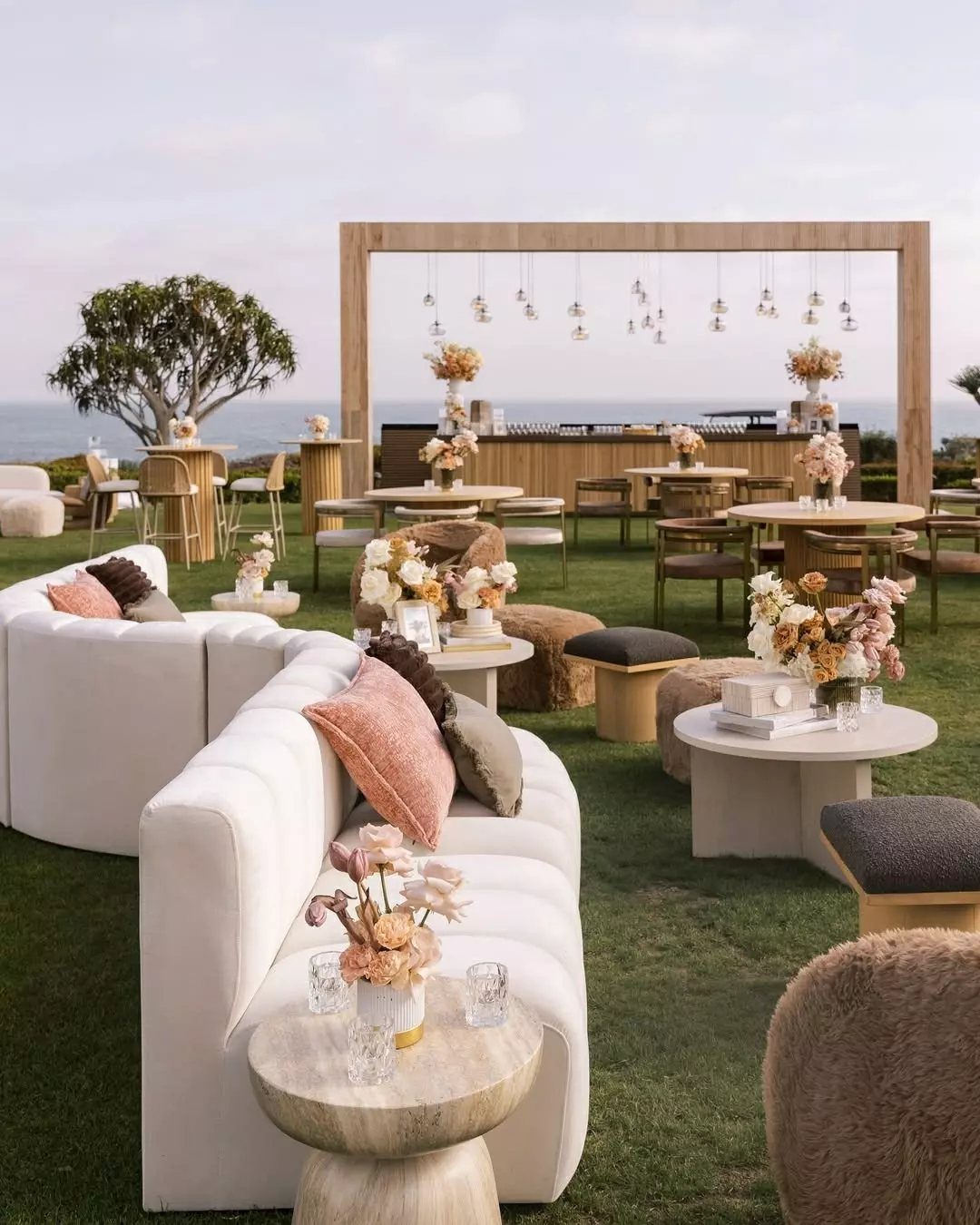 White curved sofas and textured pillows arranged around small wooden tables in an outdoor lounge.