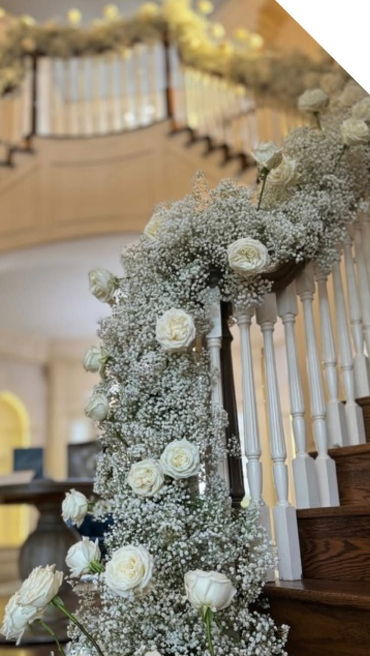 White baby's breath and roses cascading down a wooden staircase with white spindles.