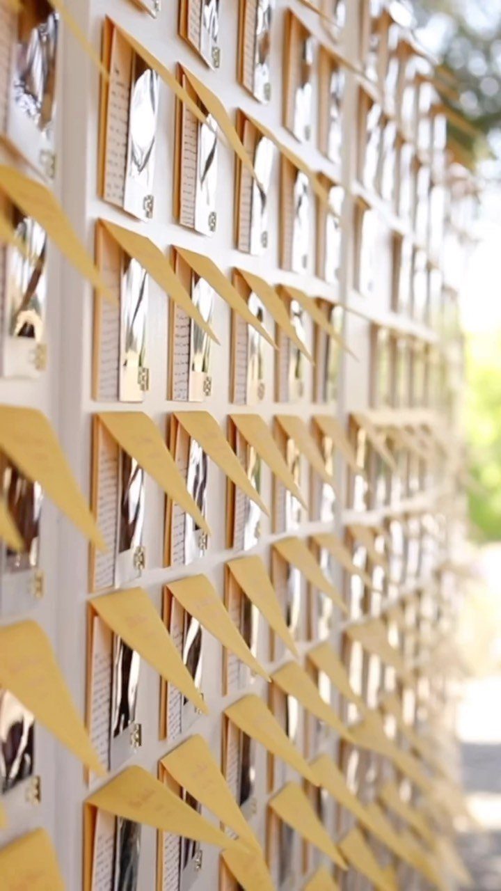 Rows of small white cards with gold accents arranged on a wall for a wedding seating chart.